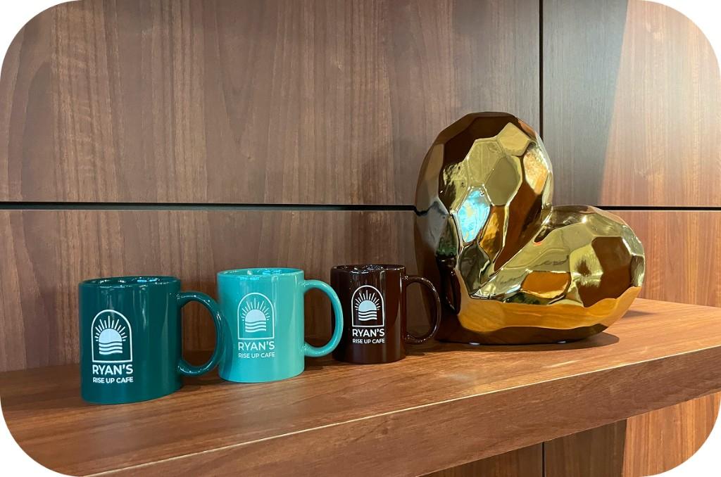 Ryan’s Rise Up Cafe mugs and heart sculpture on a shelf
